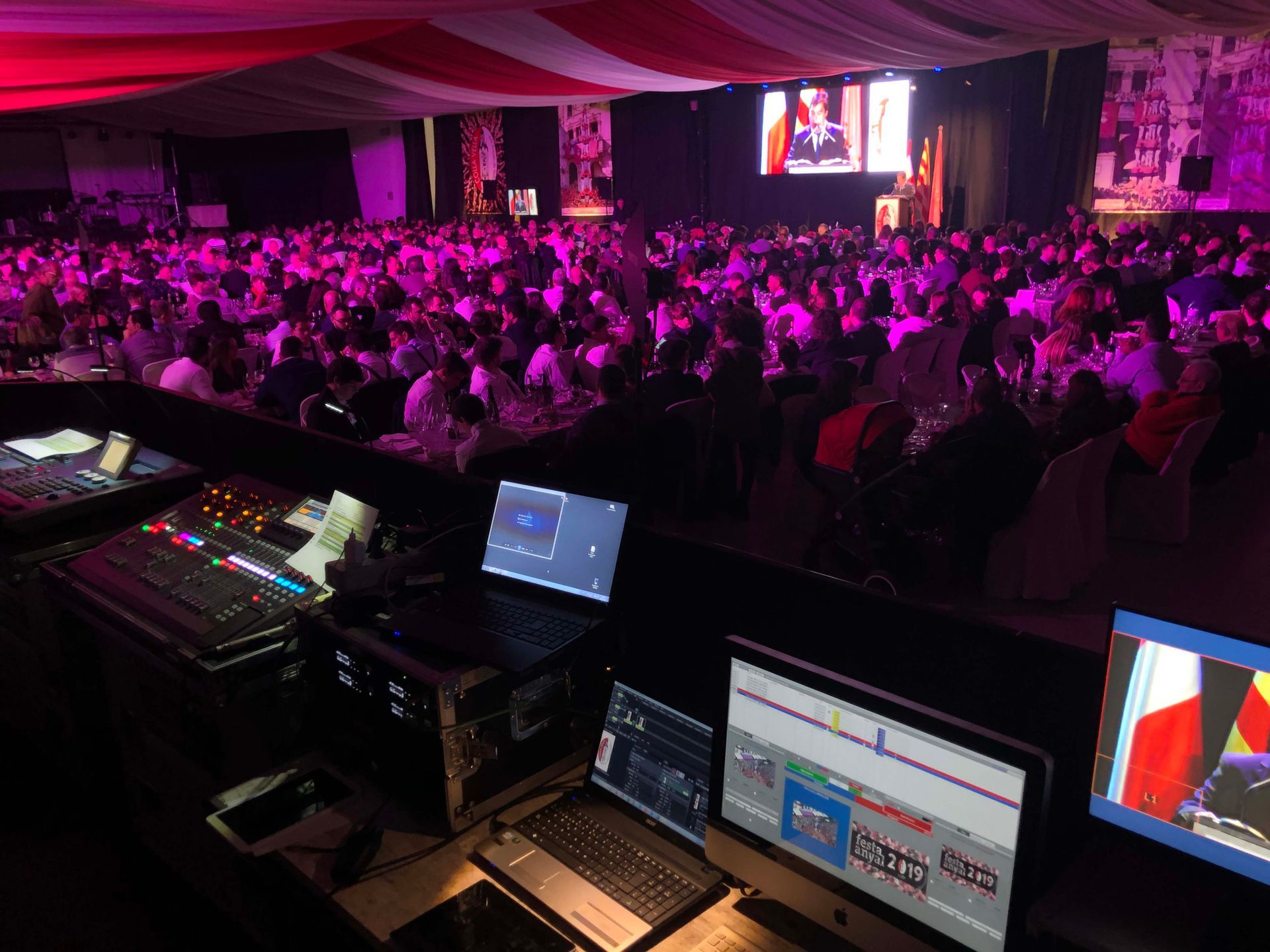 Una gran multitud de personas está sentada en una gran sala con luces violetas.