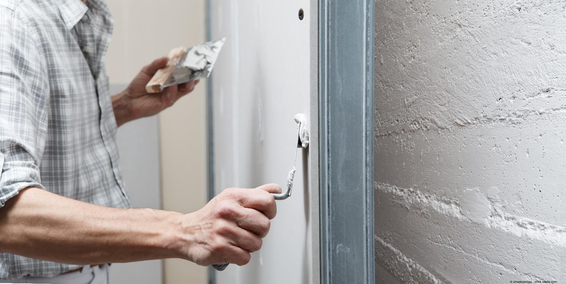Handwerker verspachtelt eine Trockenbauwand im Innenbereich mit einer Spachtel.