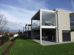 Immeuble moderne de deux étages avec balcon vitré donnant sur une pelouse verdoyante sous un ciel partiellement nuageux.
