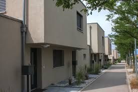 Rangée de maisons modernes couleur sable avec des étages supérieurs carrés, un trottoir et des arbres.