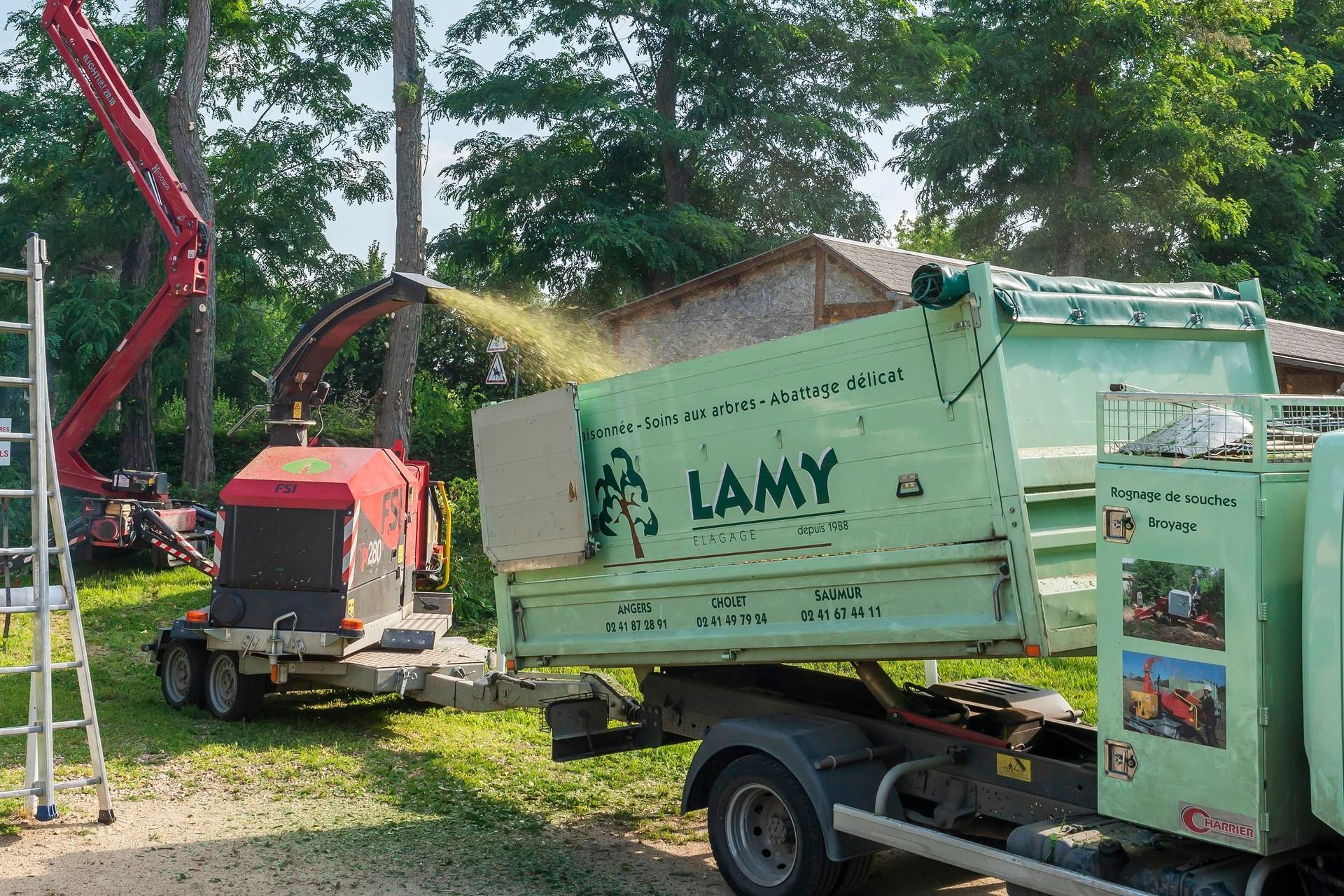 Une broyeuse en fonctionnement à côté d'un camion benne de Lamy Élagage
