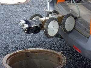 Ein Roboter sitzt neben einem Kanaldeckel.