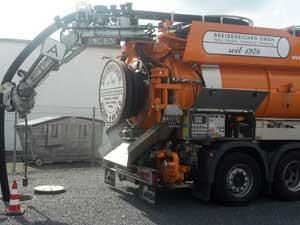 Auf einem Parkplatz steht ein großer orangefarbener Saugwagen.