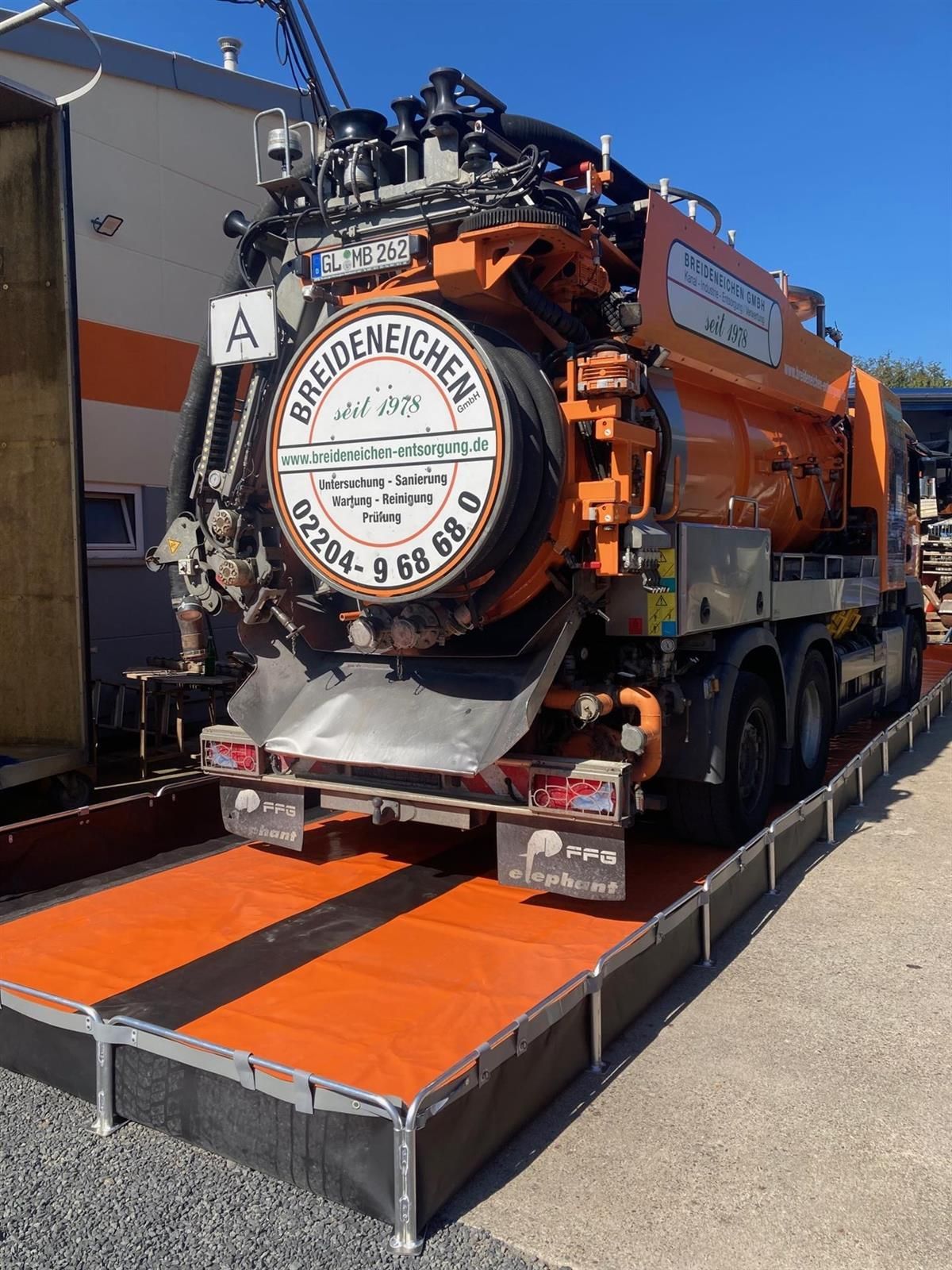 Ein großer orangefarbener Lastwagen steht auf einer orangefarben-schwarzen Plattform.