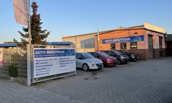 Gebrauchtwagenhändler mit draußen geparkten Autos und einem großen Verkaufsschild vor einem Backsteingebäude.