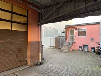 Ein leerer, gepflasterter Innenhof mit einem rosafarbenen Gebäude, einer Treppe und einem braunen Garagentor unter einem überdachten Dach