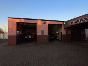 Außenansicht der Bridgestone-Autowerkstatt bei Sonnenuntergang, mit offenen Garagenplätzen und Autos im Inneren