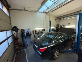Schwarze Limousine auf einer Hebebühne in einer hellen Autowerkstatt mit offenem Rolltor