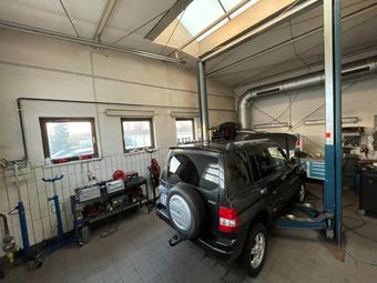 Dunkler SUV in einer Hebebühne in der Garage, mit Werkzeug und Dachfenstern