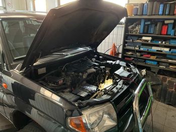 Schwarzer SUV mit geöffneter Motorhaube in einer Garage, Motor freiliegend, Werkzeug auf Regalen daneben.