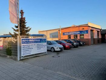 Parkplatz eines Autohauses mit geparkten Autos und einem Schild mit der Aufschrift „AUTO-MOTIVATION“ unter klarem Himmel.