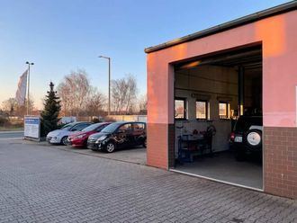 Parkplatz mit mehreren Autos neben einer offenen Werkstatt bei Sonnenuntergang