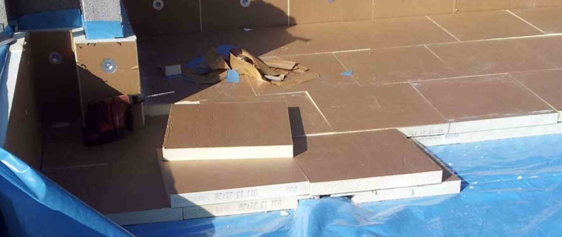 Petit chien sur une terrasse carrelée à côté de cartons et d'une piscine recouverte d'une bâche bleue