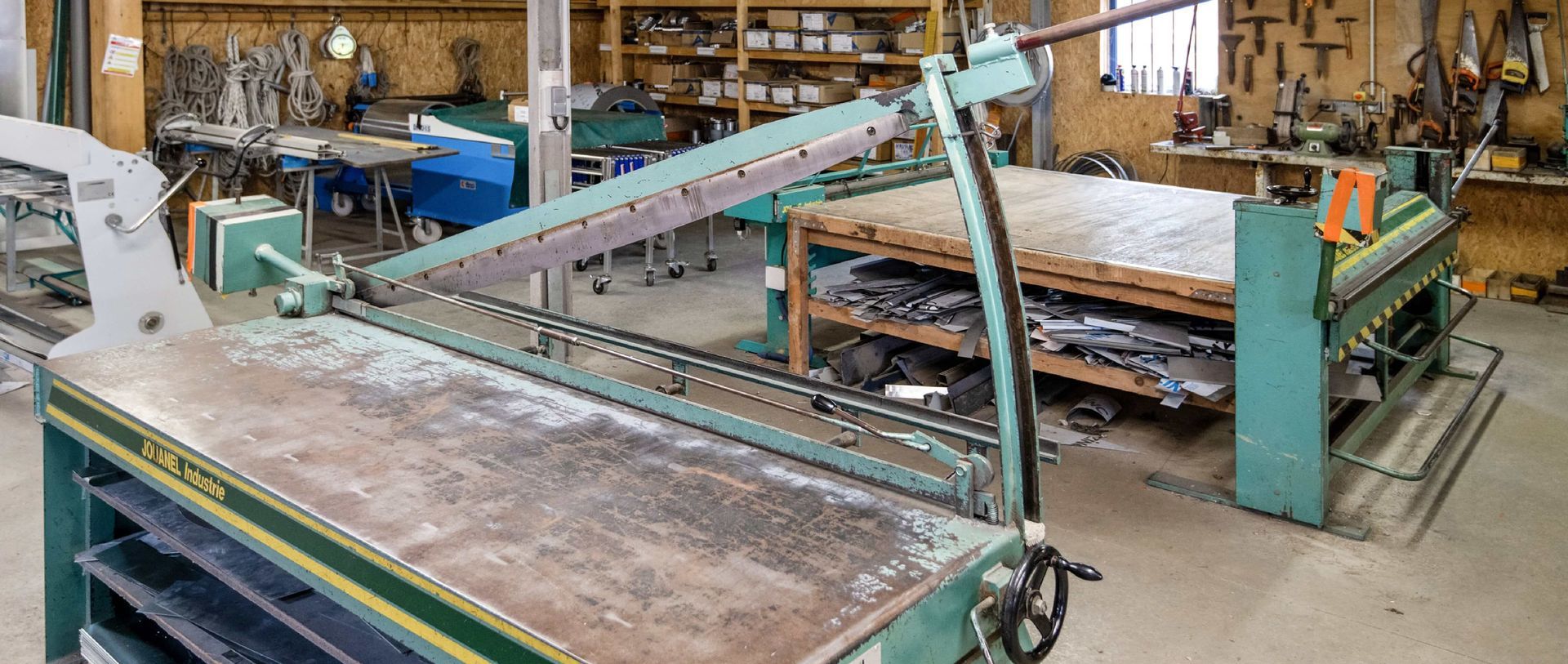 Atelier industriel équipé d'une grande machine de découpe verte et d'une longue table de travail en métal.