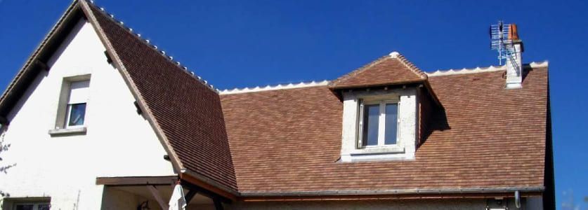 Toit d'habitation en tuiles rouge-brun avec deux lucarnes sur fond de ciel bleu