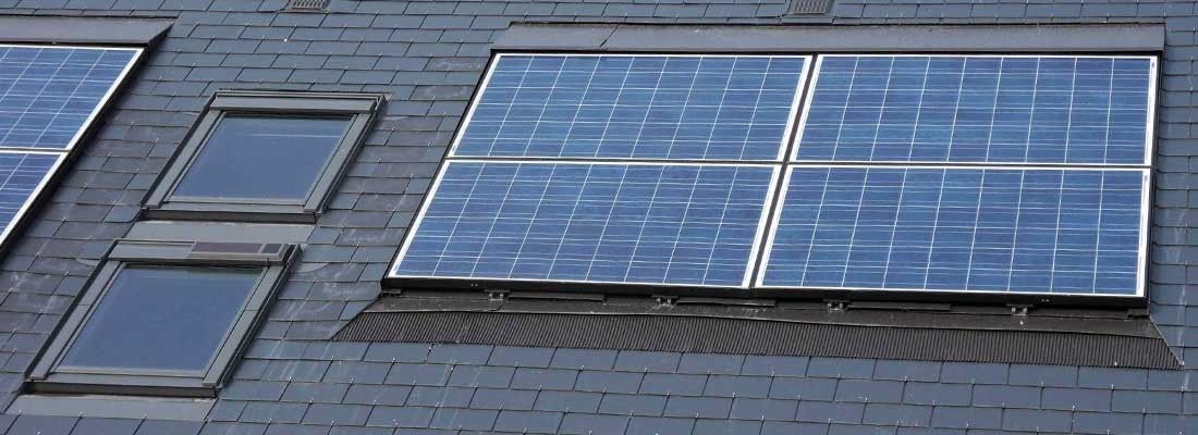 Toiture avec panneaux solaires bleus et puits de lumière sur une surface en bardeaux gris