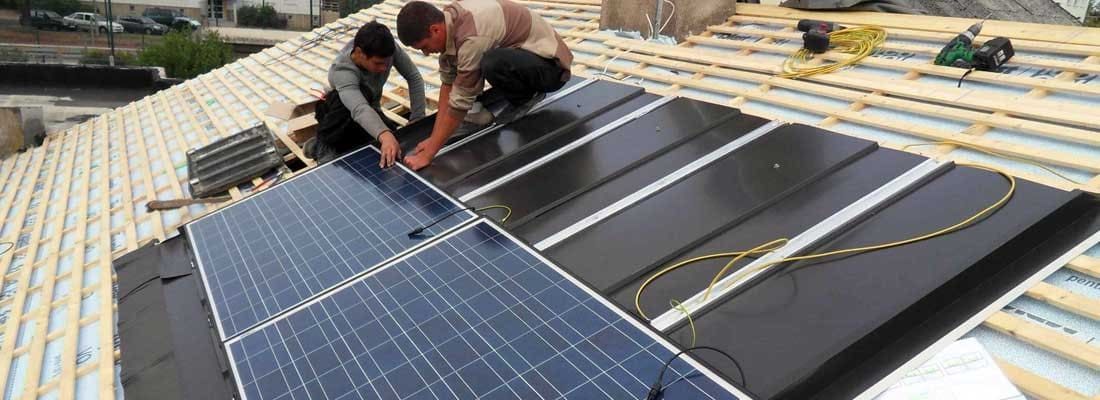 Des ouvriers installent des panneaux solaires bleus sur un toit à côté de panneaux noirs montés sur le même toit.