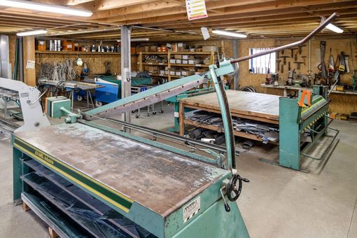Grand atelier de menuiserie avec de nombreuses machines, des outils accrochés aux murs et des piles de bois coupé sur les établis.