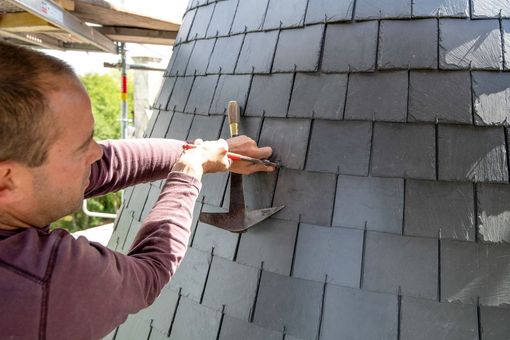 Une personne scelle une ventilation de toit sur un toit en bardeaux gris en construction