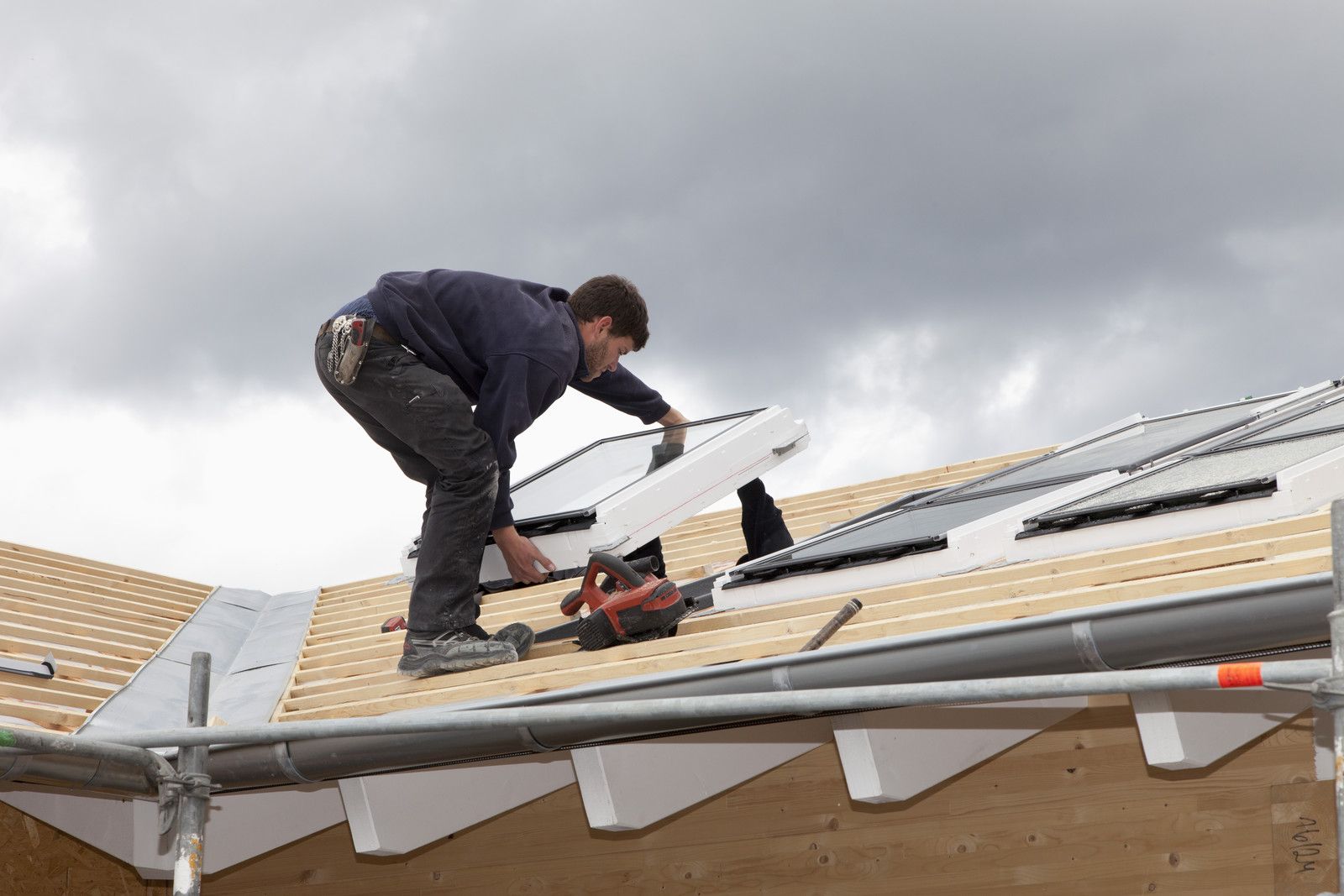 Ouvrier installant des panneaux de toiture sur le toit d'une maison sous un ciel nuageux