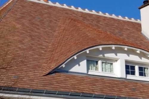 Toit de tuiles rouges avec une lucarne incurvée et des fenêtres à cadre blanc sur fond de ciel bleu