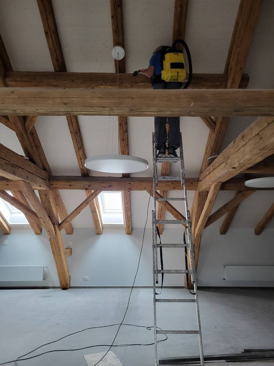 Un homme est debout sur une échelle dans une pièce avec des poutres en bois.
