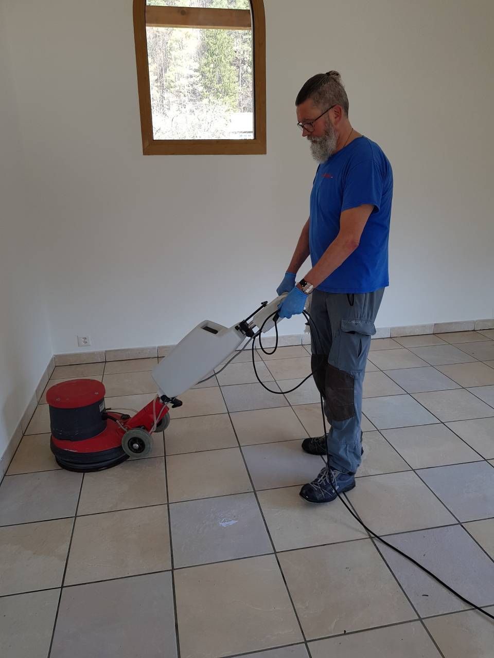 Un homme nettoie un sol carrelé avec une machine.