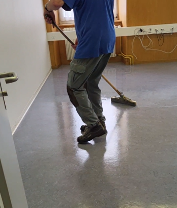 Un homme en chemise bleue nettoie le sol avec un balai.