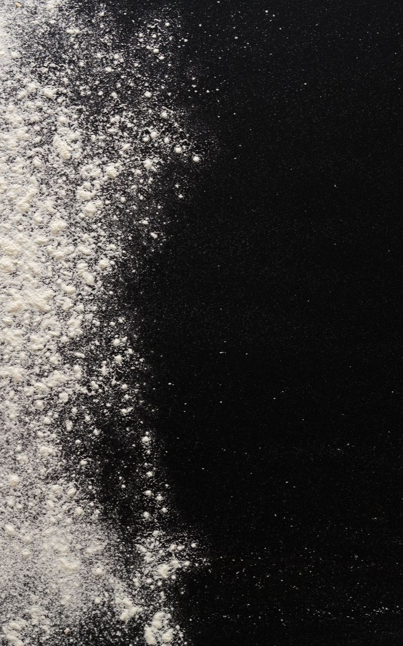 De la farine saupoudrée sur une surface noire, recouvrant le côté gauche.