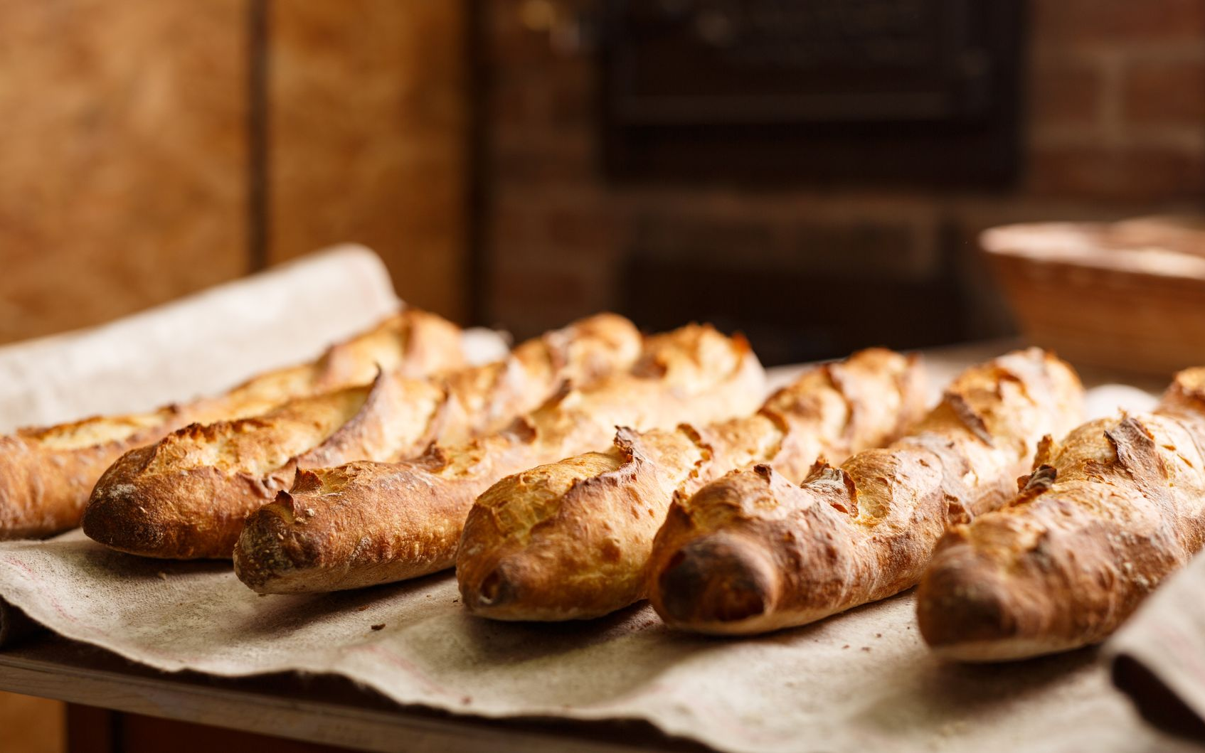 Baguettes fraîchement cuites sur du papier sulfurisé, devant un four à briques.