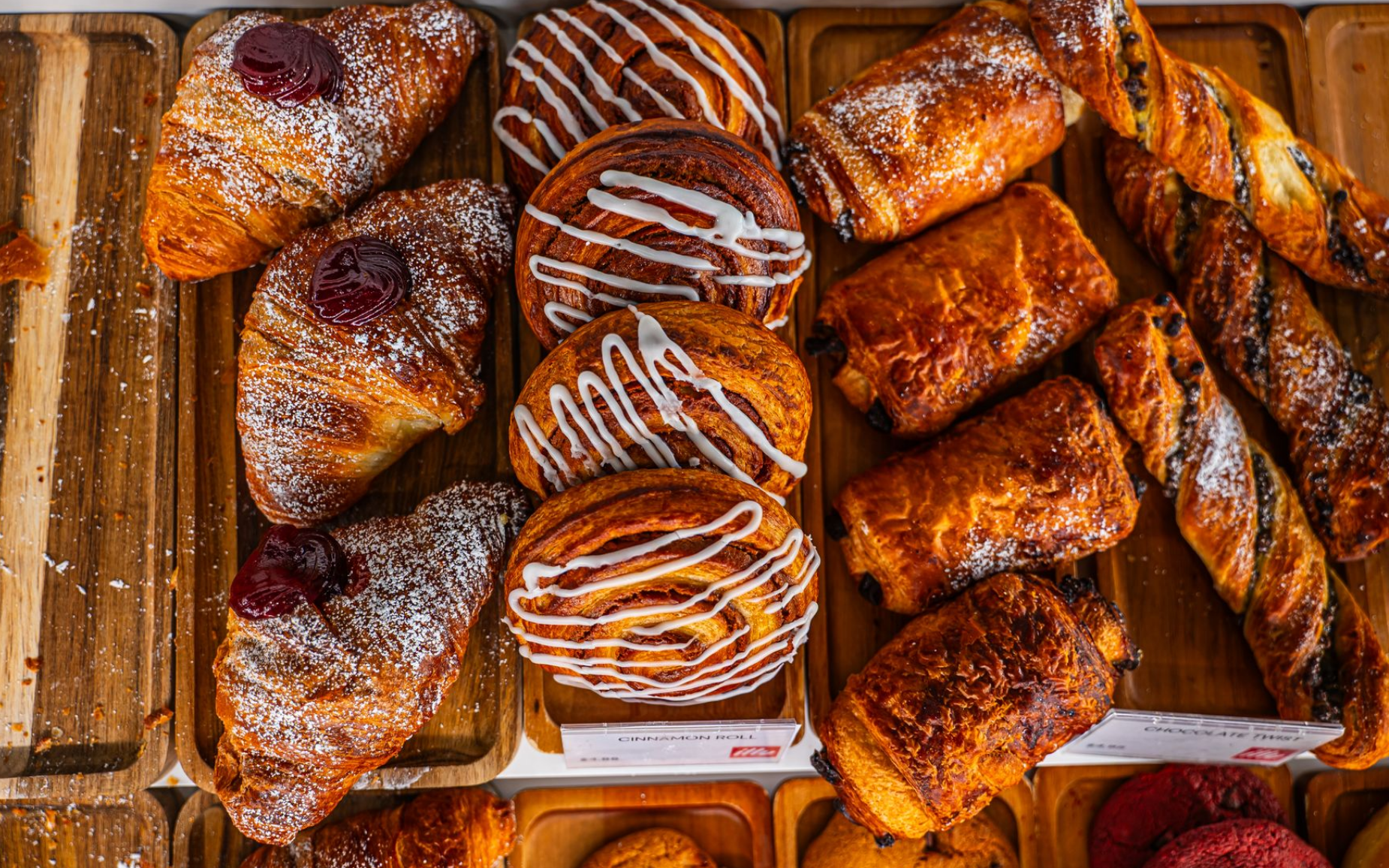 Assortiment de viennoiseries : croissants, viennoiseries et torsades, sur des plateaux en bois.