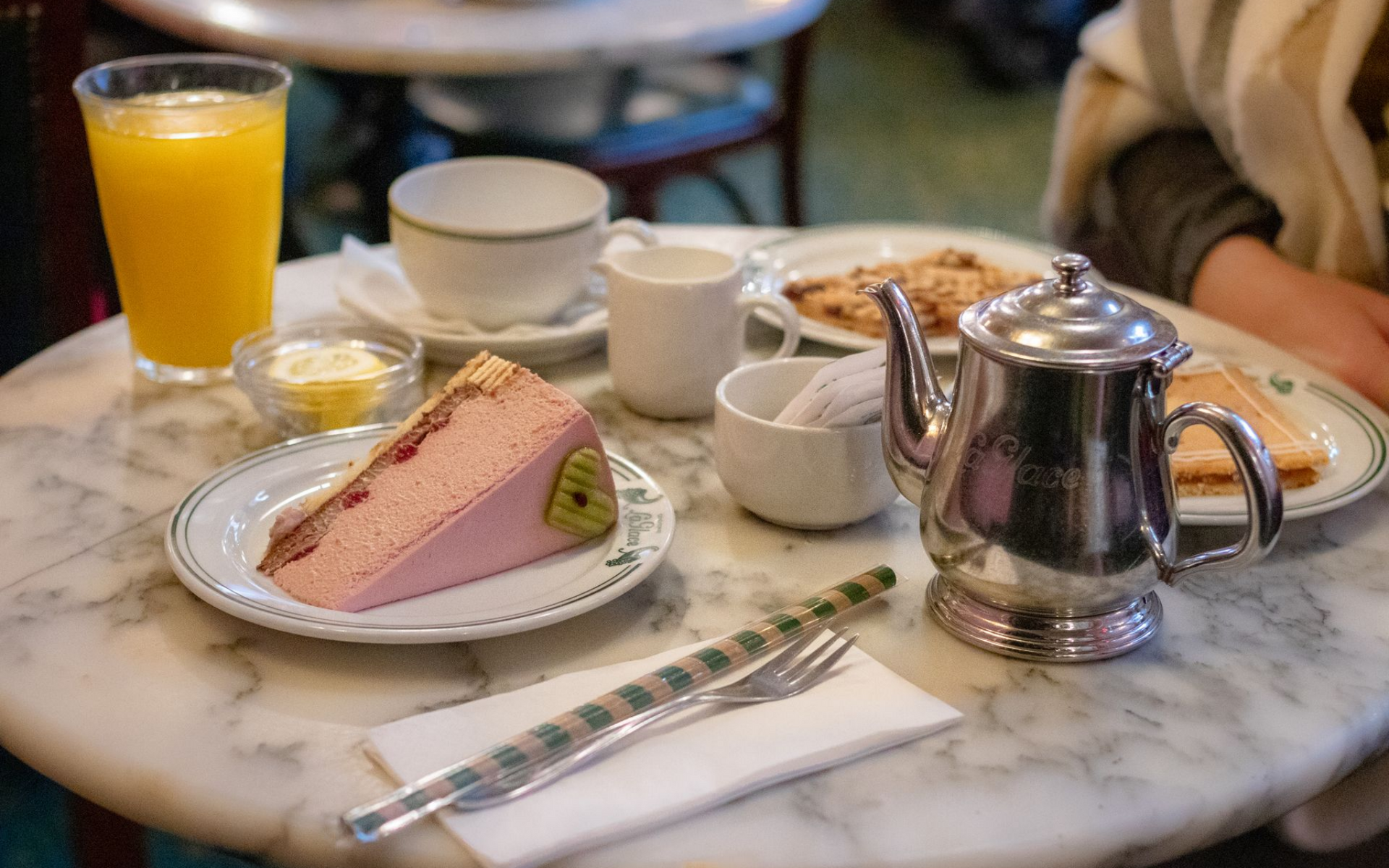 Petit-déjeuner composé d'une part de gâteau rose, de jus d'orange, de thé, de pain grillé, de marmelade et de couverts sur une table en marbre.