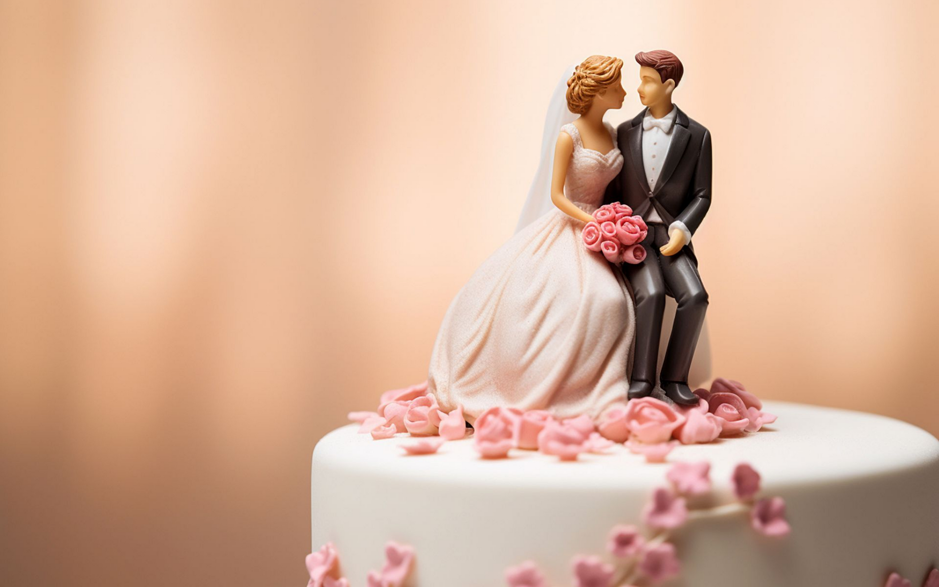 Gâteau de mariage orné de figurines de mariés, de fleurs roses, de glaçage blanc. Fond pêche.