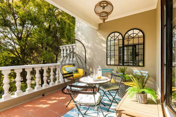 Firenza Sandton Accommodation Balcony with hanging chair, small table with chairs, and arched mirrors, surrounded by trees.