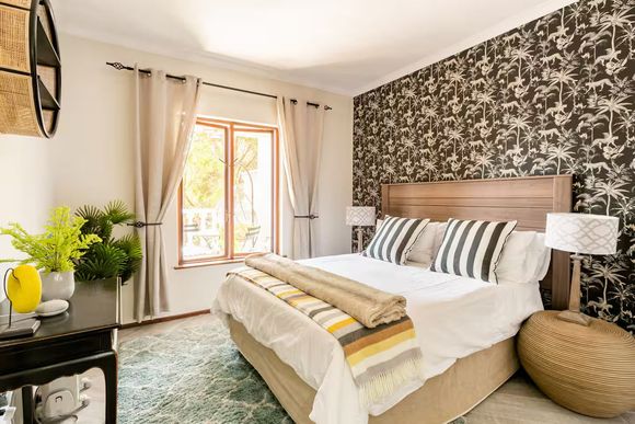 Firenza Sandton Accommodation. Bedroom with patterned wallpaper, wooden headboard, and tan curtains.
