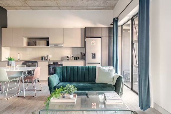Sandton Accommodation Lineal Modern open-plan apartment living space with teal sofa, kitchen, and large window.