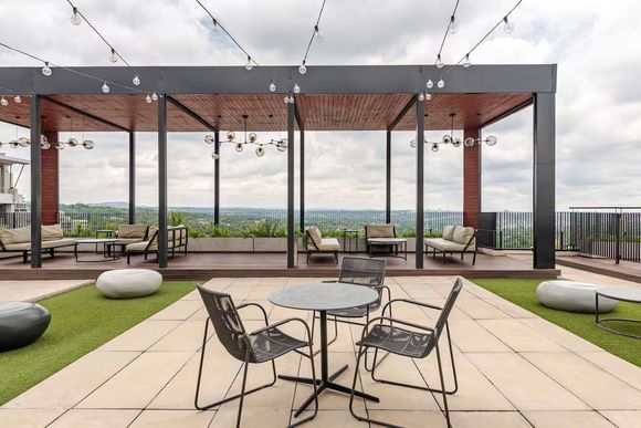 Sandton Accommodation Lineal Rooftop patio with seating, under a pergola with string lights. Overcast sky, cityscape view.