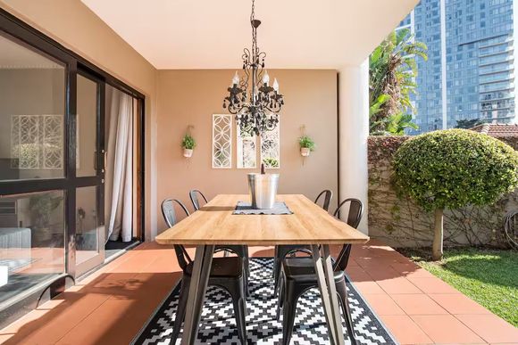 Firenza Sandton Accommodation. Outdoor dining area with wooden table, black chairs, and a chandelier.