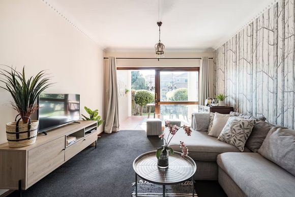 Firenza Sandton Accommodation Living room with grey sofa, TV, and sliding glass door to a patio with garden