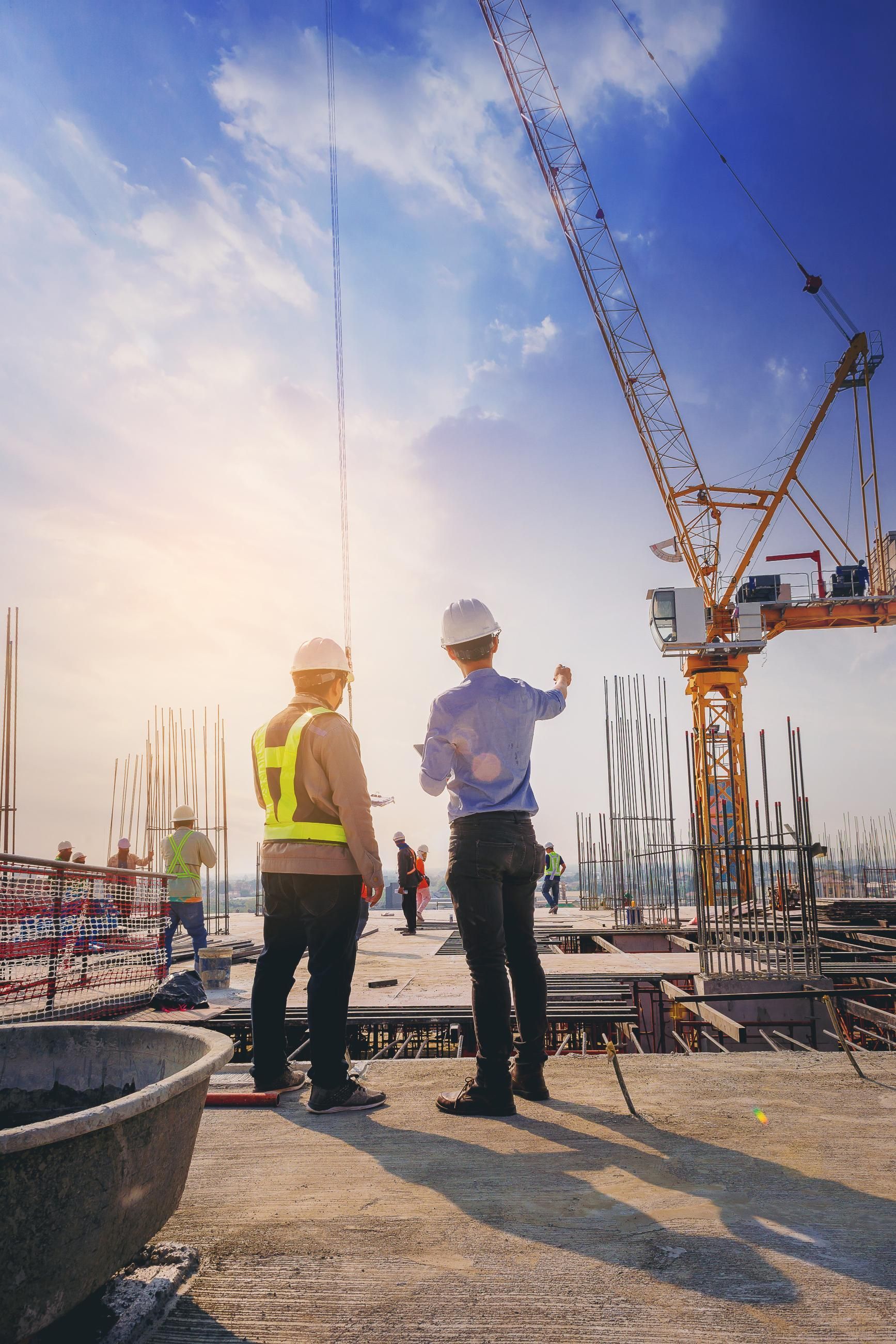 Zwei Bauarbeiter stehen auf einer Baustelle und schauen auf einen Kran.