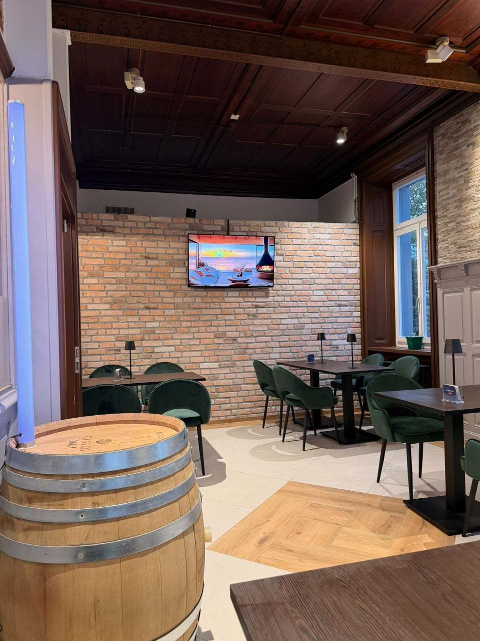Gemütliche Bar mit Backsteinwänden, grünen Stühlen, einem Holzfasstisch und einem an der Wand montierten Fernseher in einem ungezwungenen Essbereich
