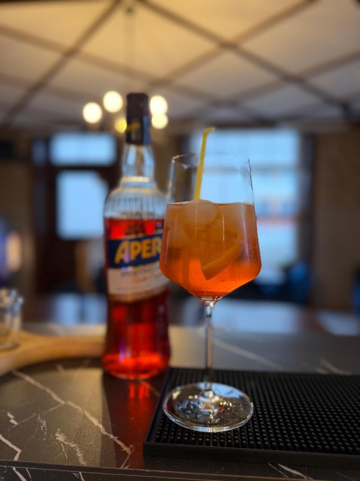 In einer schwach beleuchteten Bar heben Hände bunte Cocktails in die Höhe, im Hintergrund sind Flaschen verschwommen zu erkennen.