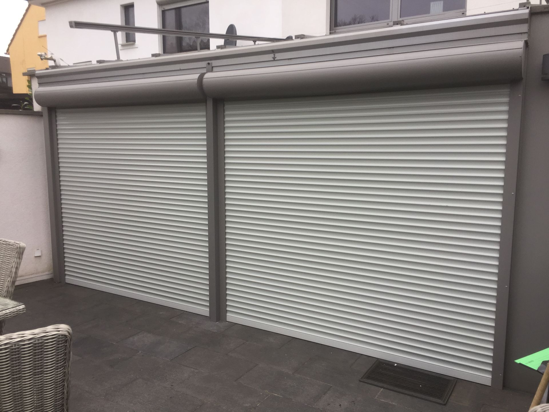 Zwei graue Rollläden verdecken die Terrassentüren einer Terrasse.