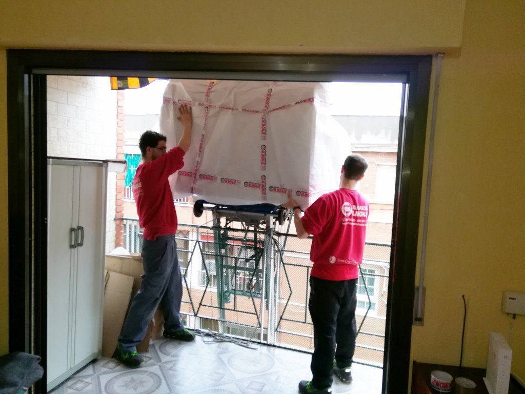 Dos hombres llevan una gran caja blanca en un balcón.