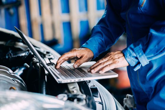 Homme avec son PC portable sur un moteur de voiture