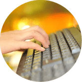 Mano escribiendo en un teclado de computadora gris con un fondo amarillo anaranjado borroso.