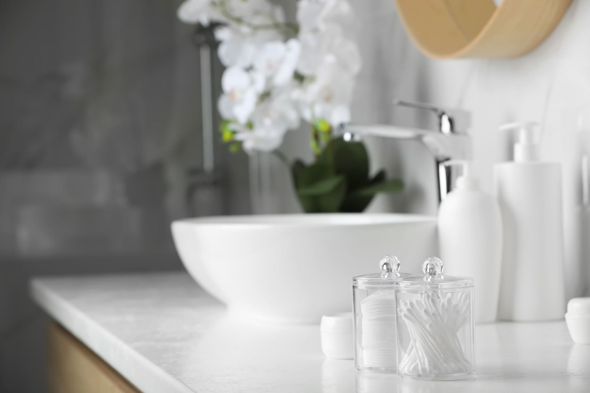 Un baño con lavabo, dispensadores de jabón, hisopos de algodón y un jarrón de flores.