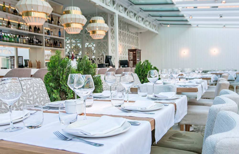 Un restaurante con muchas mesas y sillas y platos y vasos encima.