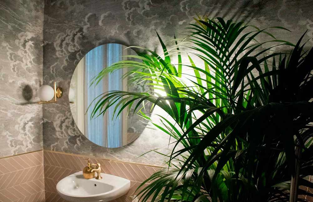 Un baño con lavabo, espejo y palmera.