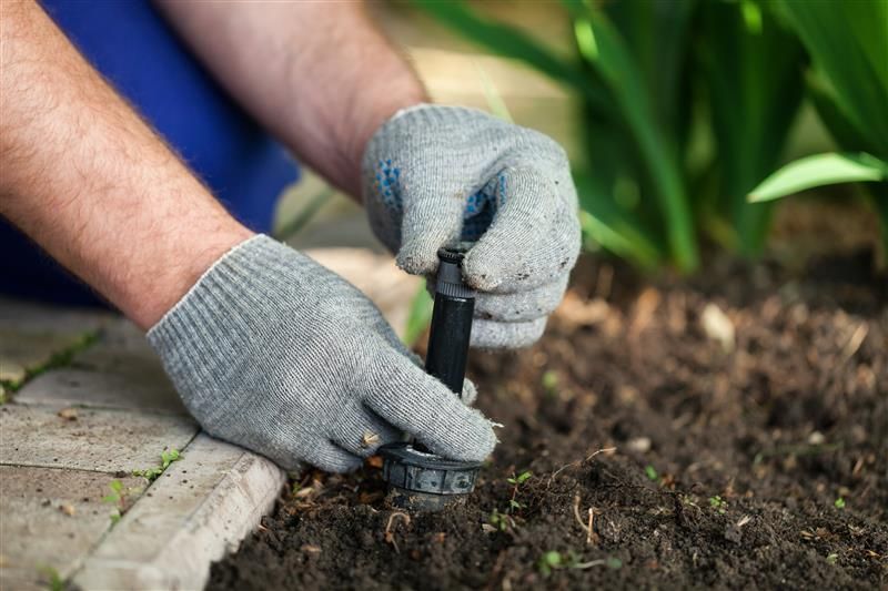 Des mains interviennent sur un système d'arrosage